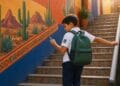 Imagen ilustrativa de un estudiante con mochila que consulta un celular en unas escaleras